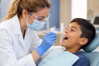 Pediatric Dentist Examining Young Boy Teeth in Clinic Stock Photo